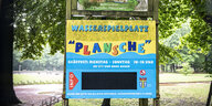 Ein Schild mit der Aufschrift "Wasserspielplatz Plansche" weißt auf die Öffnungszeiten des Spielplatzes hin