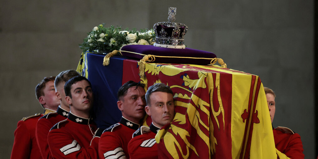 Männer in roten Uniformen tragen den Sarg der Königin, auf dem Blumen und die Krone liegen