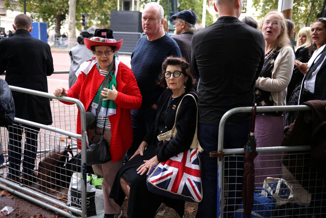 Frauen mit Union-Jack-Hüten und Taschen warten hinter einer Absperrung