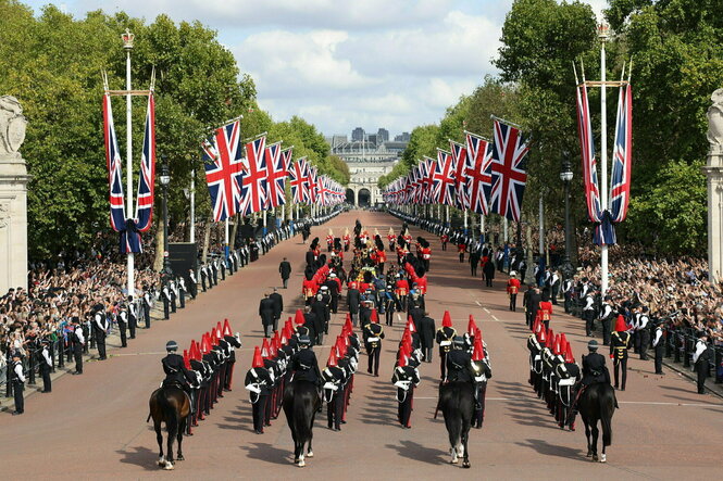 Männer in Uniformen und Pferde begleiten den Sarg der Königin auf der Allee richtung Westminster Hall, flankiert von Flaggen und vielen Zuschauern