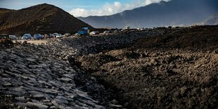 Vulkangestein, im Hintergrund Autos und Berge