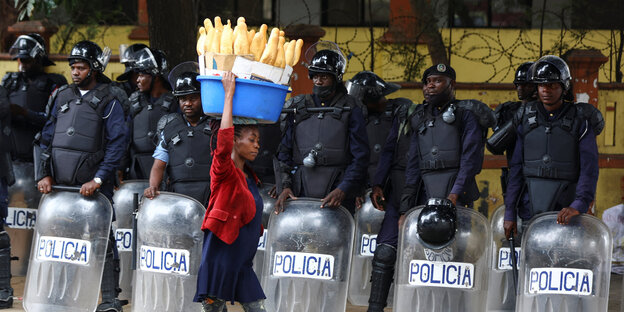 Eine Frau trägt Brote auf dem Kopf, sie läuft an einer Polizeikette vorbei