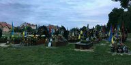 Grabsteine mit ukrainischen und rotschwarzen Flaggen auf einem Friedhof