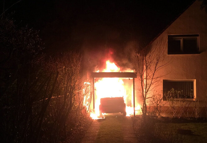 Nächtliche Szene eines brennenden Autos neben einem Wohnhaus