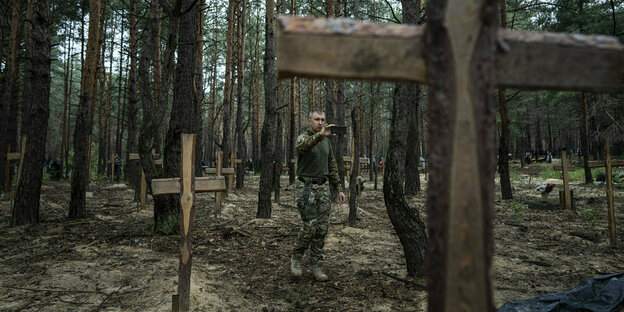 A man stands between graves marked with wooden crosses