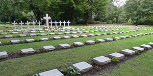Mehrere Reihen weißer Kissensteine mit zehn großen Granitkreuzen im Hintergrund