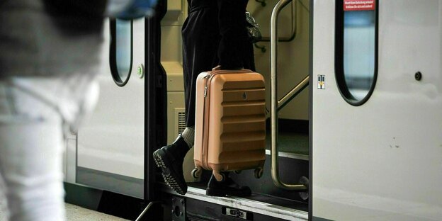 Jemand steigt mit dem Koffer in der Hand die Stufen hoch in einen Zug der Deutschen Bahn