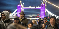 Menschen stehen Schlange, im Hintergrund die abendlich beleuchtete Tower Bridge