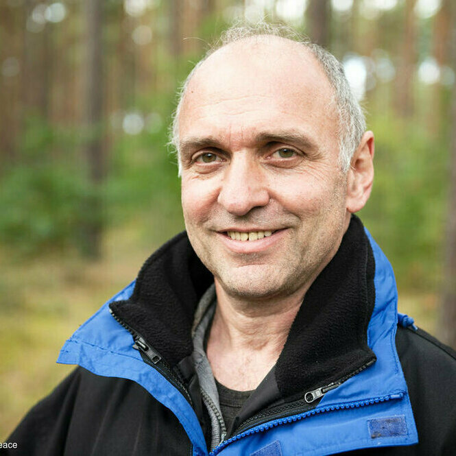 Der Forscher lächelt, steht in einem Wald und hat eine Glatze