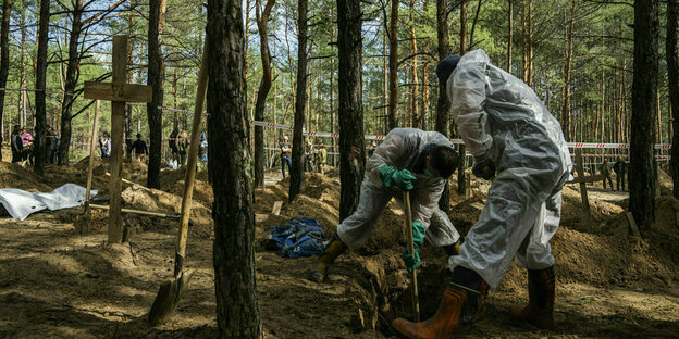 Personen in weißen Plastikanzügen exhumieren Leichen in einem Wald