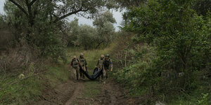 Vier Soldaten in Kampfmontur tragen einen schwarzen Leichensack auf einem Waldweg