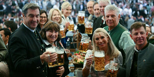 Markus Söder in Gesellschaft anderer Biertrinker hebt im Bierzelt sein Glas