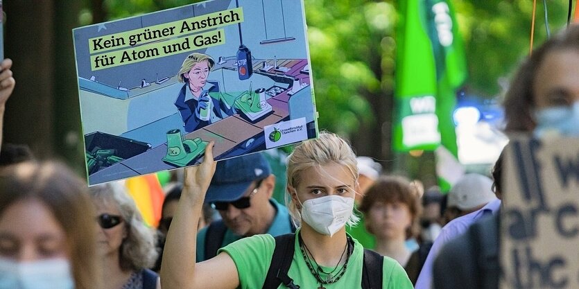 Eine junge Frau hält ein Protestplakat gegen Taxonomie in den Händen