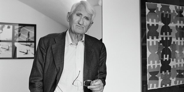 Habermas leans against a post in a jacket and open shirt