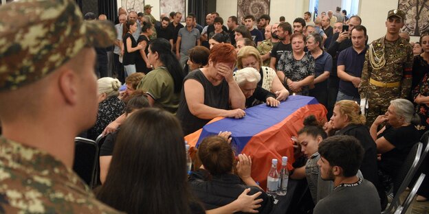 Trauernde Menschen stehen um einen Sarg, der mit der armenischen Flagge bedeckt ist