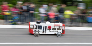 Eine Seifenkiste in der Form eines Stadtwerke Buses fährt bei einem Seifenkistenrennen auf einer Straße.