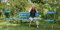 Eine Frau sitzt im Garten auf einer Bank und setzt sich gerade die Brille auf