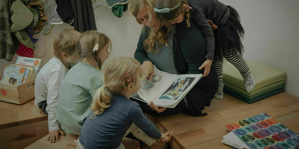 Kinder umringen eine Person, die aus einem Buch liest