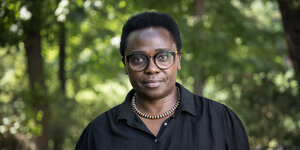 Ein Foto der ugandischen Schriftstellerin Jennifer Nansubuga Makumbi. Sie trägt eine Brille und eine Halskette und schaut ernst in die Kamera
