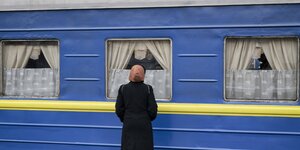 Eine Frau steht auf einem Bahnsteig vor einem blau-gelben Waggon der ukrainischen Eisenbahn.