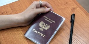 Eine Hand hält einen russischen Pass, ein Stft liegt auf dem Tisch