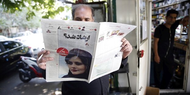 A man reads an Iranian daily newspaper.  On the cover is a portrait photo of Mahsa Amini