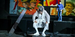 Ein Mann in futuristisch weißem Anzug steht schreiend auf der Bühne