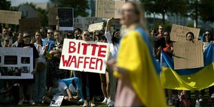 Demonstration mit Ukrainischen Fahnen und einem Schild mit der Aufschrift "Bitte Waffen"