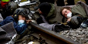 drei junge Menschen klammern sich liegend an Bahngleise