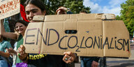 Demonstrantin hält ein Pappschild mit der Aufschrift "End Colonialism" hoch