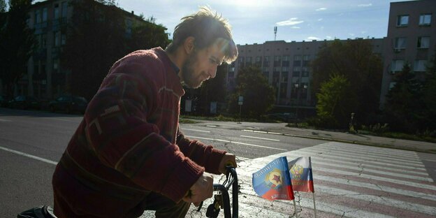 Eine Person auf einem Fahrrad, dass mit den Fahnen Russlands und Luhanks geschmückt ist