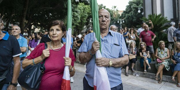 Ein älteres Paar trägt je eine zusammengerollte Fahne Italiens. Die Mienen der beiden sind ernst