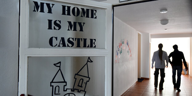 Auf einer Tür eines Wohnheims für minderjährige Geflüchtete steht "My Home is my castle"; rechts im Hintergrund sieht man zwei Jugendliche einen Flur entlanglaufen