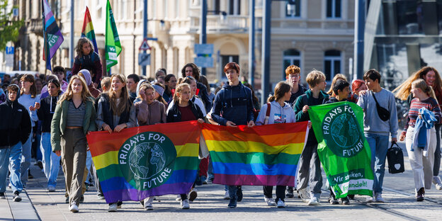 You can see young demonstrators walking towards the camera on the street.  They hold rainbow flags.  One has a green round print that says Fridays for Future.