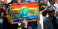 Eine Frau nimmt an einer Demonstration zum globalen Klimastreik teil und hält ein Plakat mit der Aufschrift ·Help Her· neben einem Bild der Erde in den Händen