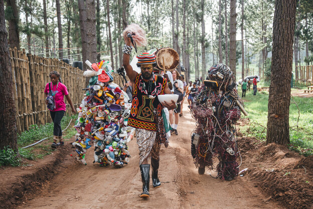 Menschen in z.T. aus Müll gefertigten Kostümen laufen einen Waldweg entlang