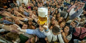Ein junger Mann hebt aus einer Menschenmasse ein Maß Bier in die Luft