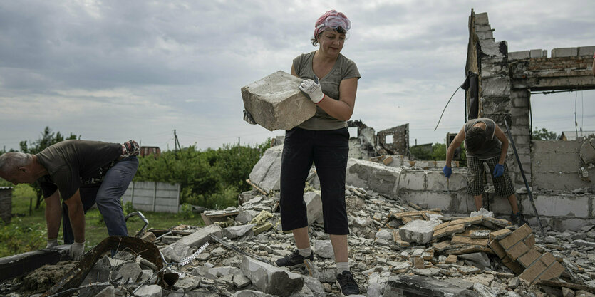 Ein Mann, eine Frau und ein Junge räumen den Schutthaufen weg, der ein Haus war. Es wurde durch russische Bombardierung zerstört wurde