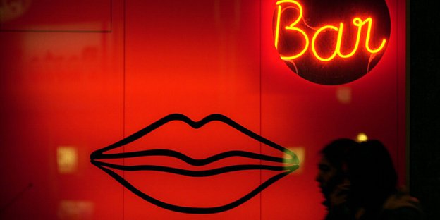 Passanten gehen in Frankfurt/Main an einer Erotik-Bar vorbei, die im rot beleuchteten Schaufenster mit übergroßen Lippen wirbt.
