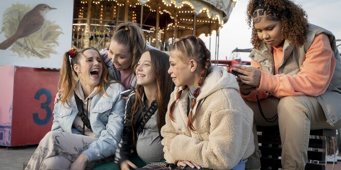 Minderjährige, einige davon schwanger, sitzen lachend vor einem Karussell.