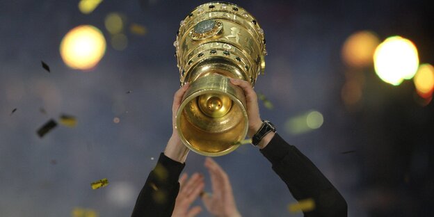 Ein DFB-Pokal wird von einem nicht sichtbaren Spieler in die Höhe gestreckt.