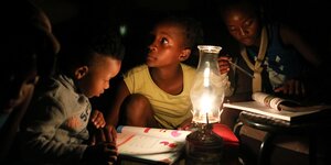 Kinder sitzen mit aufgeschlagegen Büchern im Schein einer Paraffinlampe