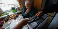 Eine alte Frau sitzt in ihrer Wohnung in Mariupol, vor ihr stehen Männer mit einer Wahlurne