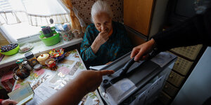 Eine alte Frau sitzt in ihrer Wohnung in Mariupol, vor ihr stehen Männer mit einer Wahlurne