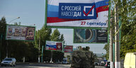 Ein Militärfahrzeug fährt vor einem Wahlplakat, auf dem "Mit Russland für immer" steht