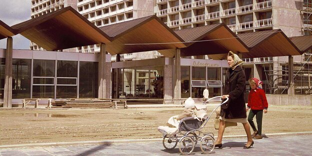 Eine Frau geht mit einem Kinderwagen vor Hochhäusern