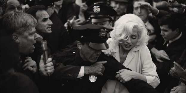 Marilyn (Ana de Armas) ist von Fans und Presse umringt, ein Polizist streckt schützend den Arm vor sie.