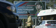 Ein Mann überquert eine Straße, hinter ihm ein Plakat, auf dem ein Soldat zu sehen ist