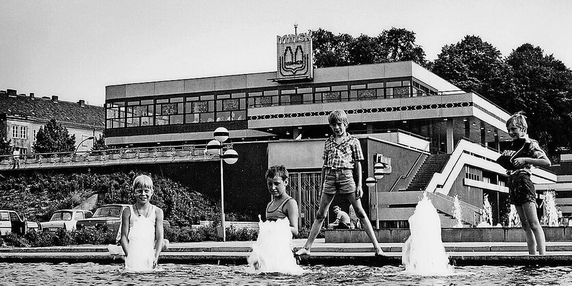 Kinder stehen in einem Wasserbecken, hinter ihnen liegt das terrassierte Gebäude des Minsk in der historischen Schwarzweißaufnahme