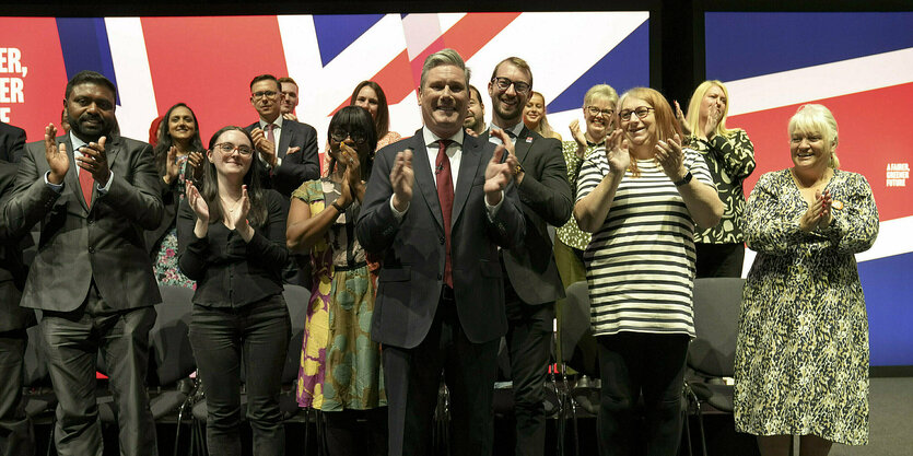 Keir Starmer applaudierend mit anderen Personen auf einer Bühne